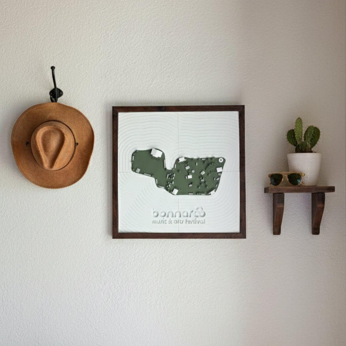 Framed bonnaroo map print on a wall with a hat and plant decor.