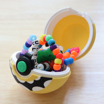 Front view of the yellow Cyclops Memory Capsule with a white eye, green center button, and toothy grin on a white display stand.