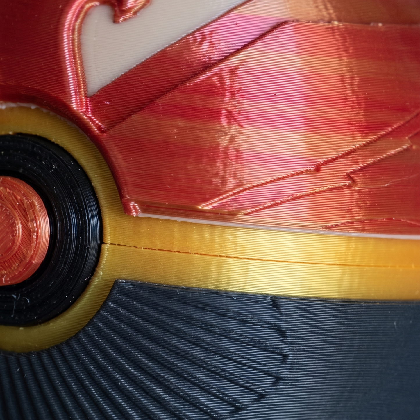 Close-up of a 3D-printed toy or prop featuring metallic red and gold wing-like patterns, a black circular element, and a textured dark gray lower section.